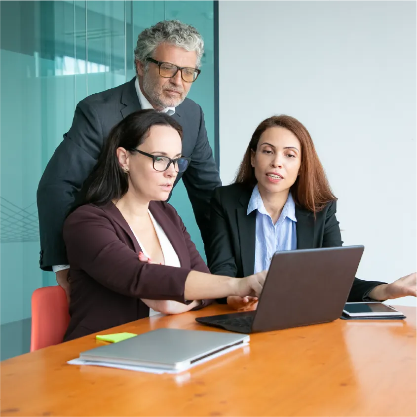 Tres directivos revisando información en una laptop dentro de una sala de juntas.