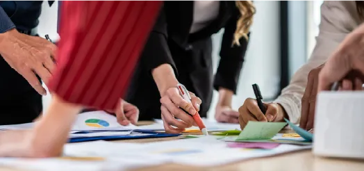 Dos personas señalando gráficas impresas sobre una mesa de trabajo.